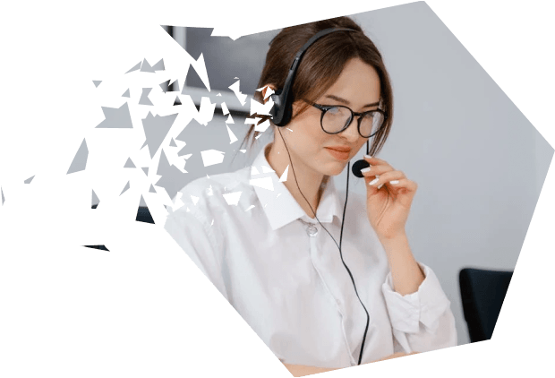 A woman wearing glasses and a white shirt, using a headset microphone while working on a laptop, sitting in an office environment.