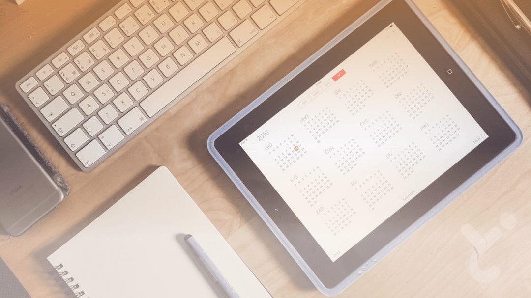 An iPad with calendar, keyboard and notebook on desk