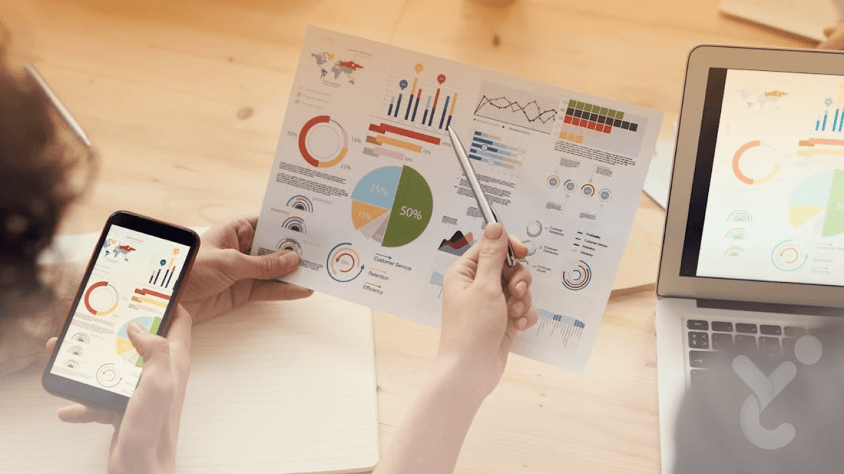 A mobile phone, laptop and a paper showing statistics with circular charts.